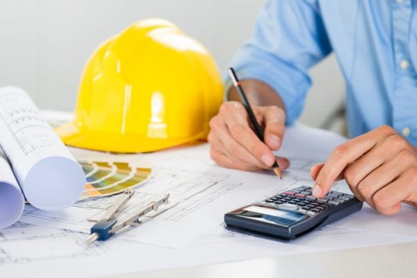 Construction Cost calculating by man sitting with yellow hard hat and blue prints